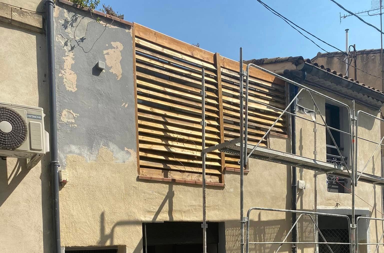 Façade de maison de ville sous échafaudage : ancien enduit gris écaillé à gauche, enduit neuf couleur sable à droite.